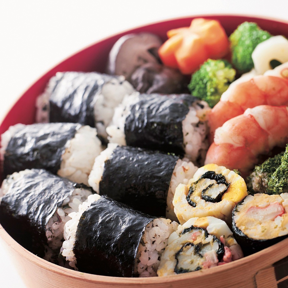 一盒木質便當盒內裝有數個以海苔包裹的飯糰，以及玉子燒、蝦子、花椰菜等配菜。