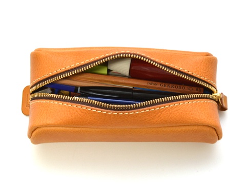 職人手作皮革圓角收納筆袋，採用淺棕色皮革製成，拉鍊部分露出多支筆、鉛筆和一支毛筆。