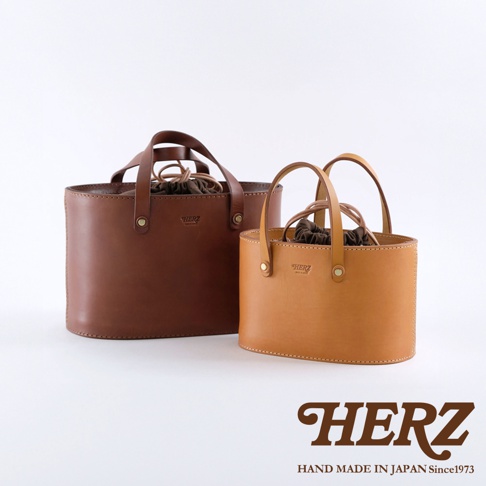 兩款職人手作皮革束口手提包，一款為深棕色，另一款為淺棕色。均採用天然皮革材質，設有束口內袋和雙提把設計。
