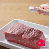 手持白色帶粉紅色透明頂蓋的leye 方便鹽匙，正在將粗鹽撒在一塊生牛肉上。牛肉置於白色長方形烤盤內，烤盤放在木質桌面。