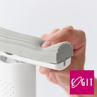 手持灰色條紋海綿刷，海綿柔軟且有彈性，刷頭邊緣帶有顆粒狀紋路，固定在白色刷柄上。