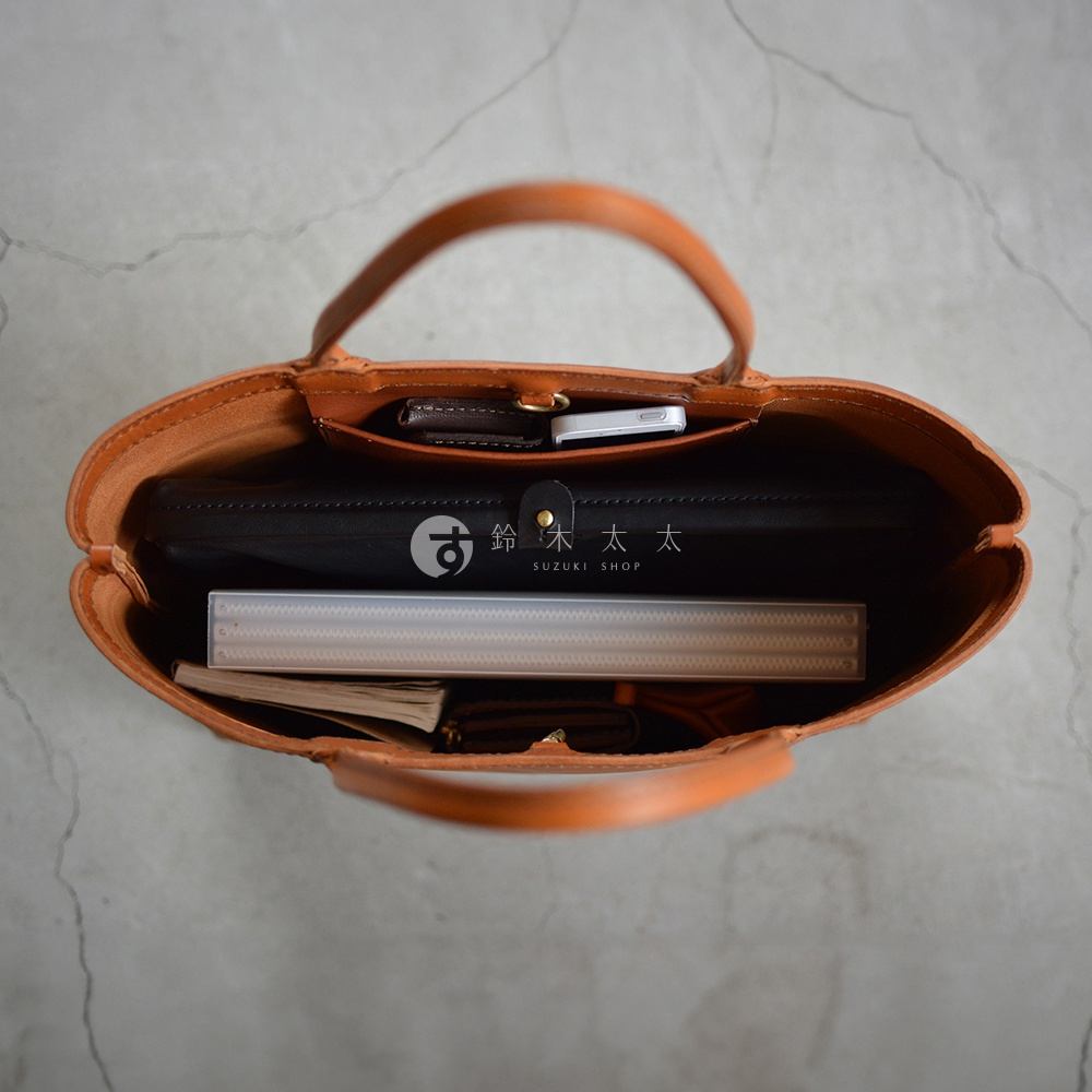 一個從上方視角拍攝的棕色皮革托特包，包內裝有手機、皮夾、筆記本和一個黑色扁平物件。