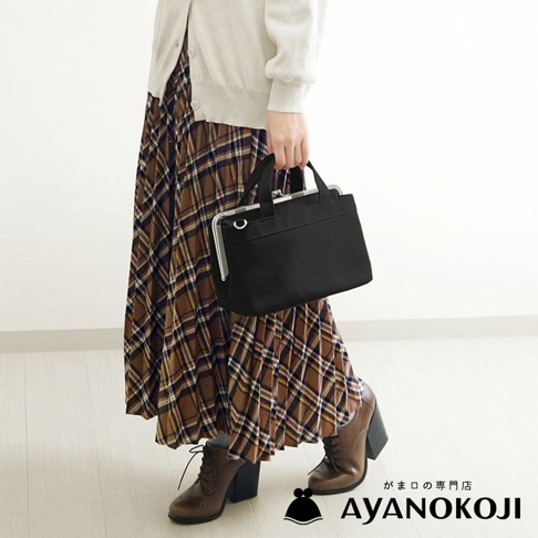 身穿格紋長裙與米白色開襟毛衣的女子，提著一個黑色橫式口金手提包。