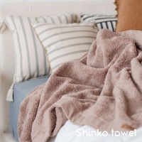 MAISON BLANC 輕奢柔膚匹馬棉浴巾，顏色為柔和的粉棕色，質地蓬鬆柔軟，呈現細膩的毛圈紋理。浴巾旁擺放著數個條紋抱枕，營造舒適居家氛圍。