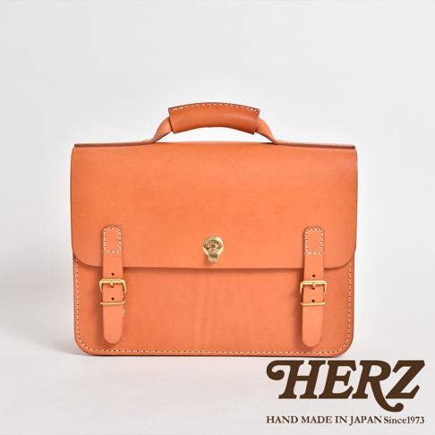橘色皮革製成的手提公事包，帶有金色旋轉鎖扣和兩個可調節皮帶扣，適合商務使用。