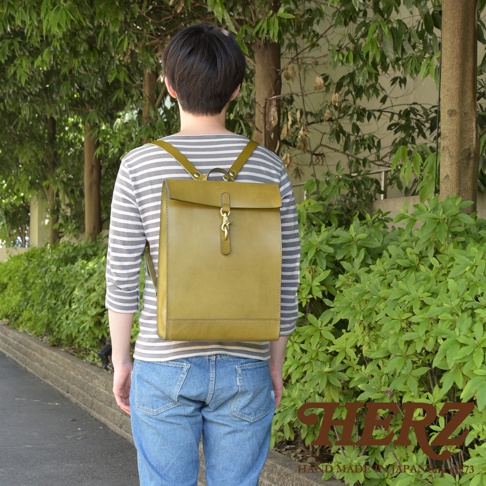 橄欖綠皮革後背包，紙袋造型，帶有金屬鎖扣，由HERZ品牌手工製作。