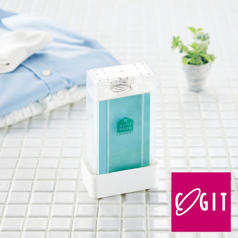 透明塑膠外殼的長方形泡沫洗衣皂盒，內含淺藍色皂盒，頂部有銀色彈簧和透氣孔。產品底部有白色底座，背景是白色瓷磚和疊放的藍色襯衫及白色襪子。
