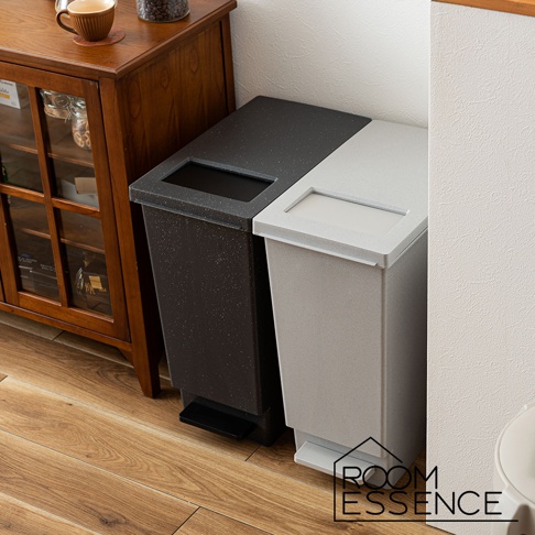 兩個附蓋簡約垃圾桶，一個為黑色帶有白色斑點，另一個為淺灰色，均配有腳踏板，可置於木質地板上，旁邊是木製櫃子。