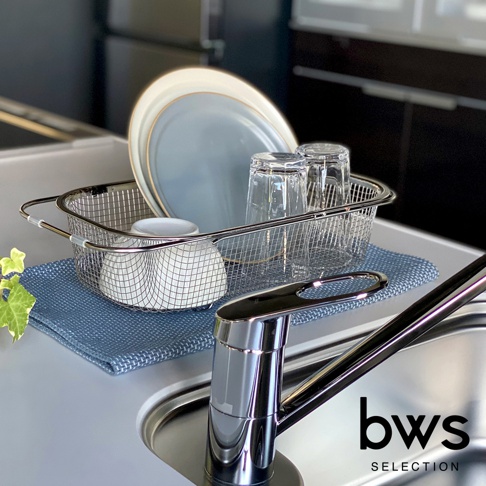 銀色不鏽鋼網狀可伸縮瀝水籃，內有藍色盤子、兩個玻璃杯和白色杯子，放置於藍色布墊上，旁邊是廚房水龍頭。