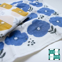 白色七層紗拭巾，印有藍色花朵、綠葉和灰色圓點圖案。另一條黃色印花拭巾疊放在上方，並以半透明紙包裝。