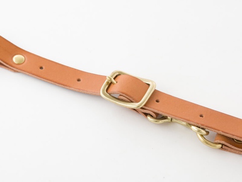 職人手作皮革背包用胸前扣帶，寬2.4cm，淺棕色皮革材質，配有黃銅色金屬扣環、調節扣和掛鉤。