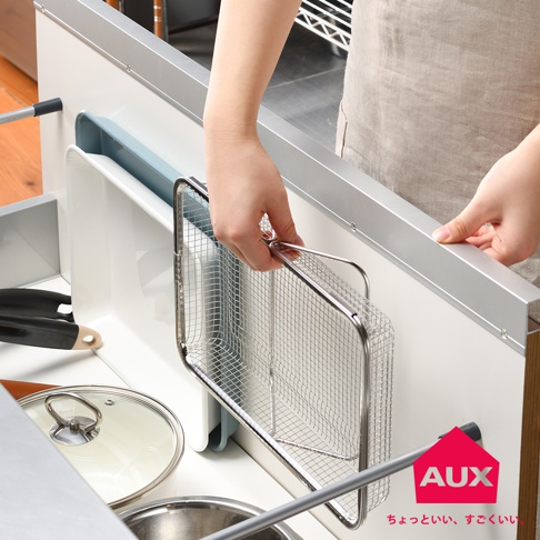 一只手正從一個灰白色抽屜中取出一個銀色金屬網狀伸縮瀝水籃。籃子是長方形的，帶有手柄。