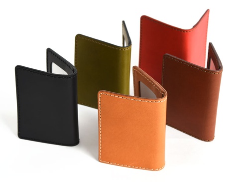 五款職人手作皮革雙折票券收納夾，顏色包含黑色、橄欖綠、橘色、紅棕色及紅色。皆為皮革材質，縫線清晰。