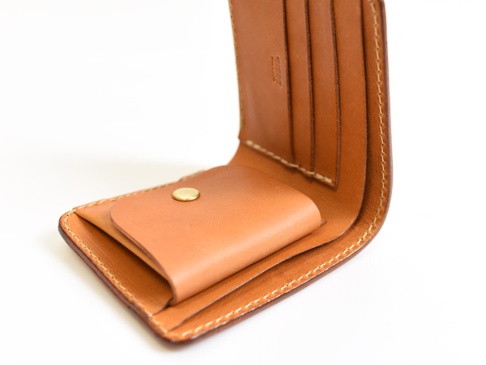 職人手作經典掀蓋扣式雙折短夾，採用棕色皮革製成，內有卡槽和零錢袋，整體呈現簡約風格。
