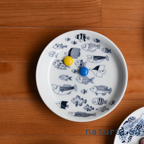 白色陶瓷小碟子，佈滿深藍色線條繪製的各種造型的魚圖案，碟子中央有兩顆分別為黃色和藍色的圓形糖果。