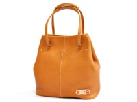 焦糖色皮革托特包，附有可調式提把，包身有縫線裝飾，底部有品牌皮革標籤。