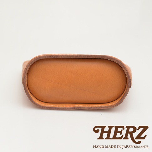 職人手作皮革收納包，呈淺棕色，可見皮革紋理及白色縫線，底部為橢圓形設計。