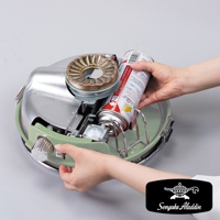 雙手正在將卡式瓦斯罐裝入淺綠色金屬材質的瓦斯暖爐主體。暖爐頂部有銀色金屬燃燒器，側邊有一個銀色旋鈕。