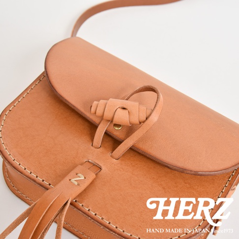 職人手作皮革流蘇側背包，採用淺棕色天然皮革製成，包蓋上有獨特的皮革繩結設計，前方裝飾有皮革流蘇。