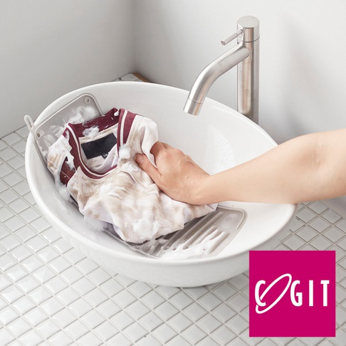 COGIT 品牌標誌下的圖片，展示了一隻手正在一個帶有排水格紋的多功能軟式洗衣板的臉盆中搓洗一件有著紅白條紋領口的白色衣物，臉盆內有許多泡沫。