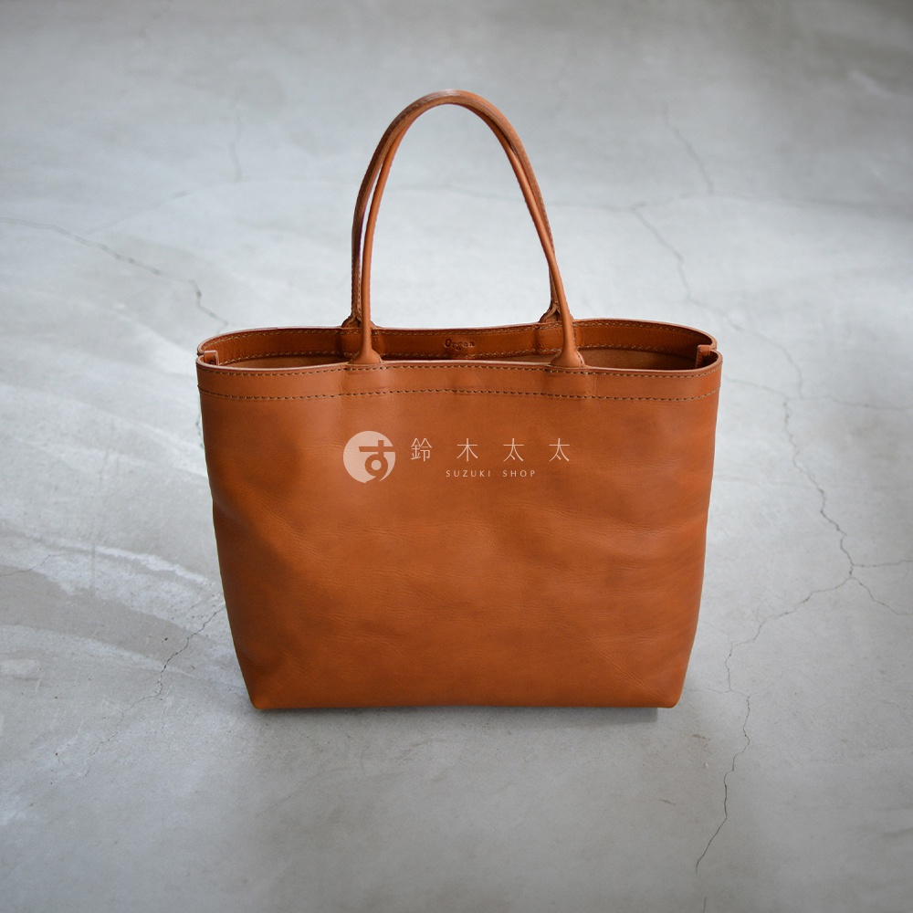 職人手作的棕色皮革托特包，包身簡潔，配有雙提把，中央印有鈴木太太SUZUKI SHOP的白色Logo。