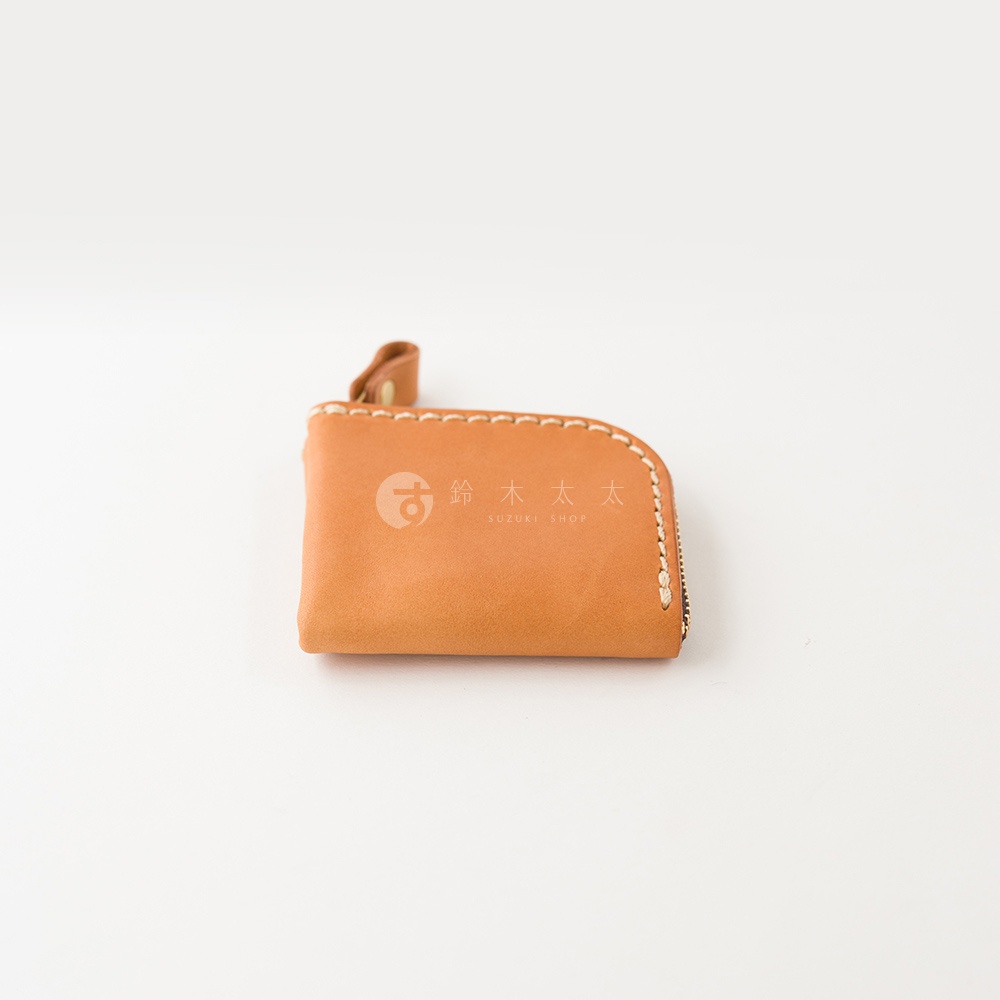 一個採用駝色Stare皮革製作的日本HERZ職人手作零錢包，外觀呈現圓潤的方形設計，邊緣以淺色線材手工縫製，上方附有皮質拉鍊環，中心印有鈴木太太標誌。