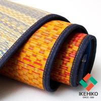 捲起的藺草瑜珈墊，表面有黃色、紅色、藍色交織的紋理，邊緣縫有深藍色滾邊。