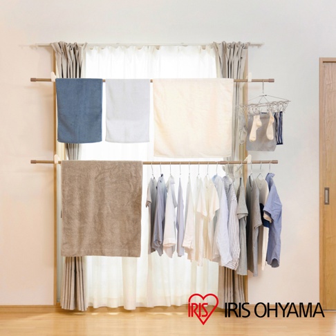 木紋頂天立地窗框曬衣架，設有兩層掛桿，上層掛有藍色、白色、米白色毛巾，下層掛有淺色系衣物，另有小型曬衣夾掛著襪子。