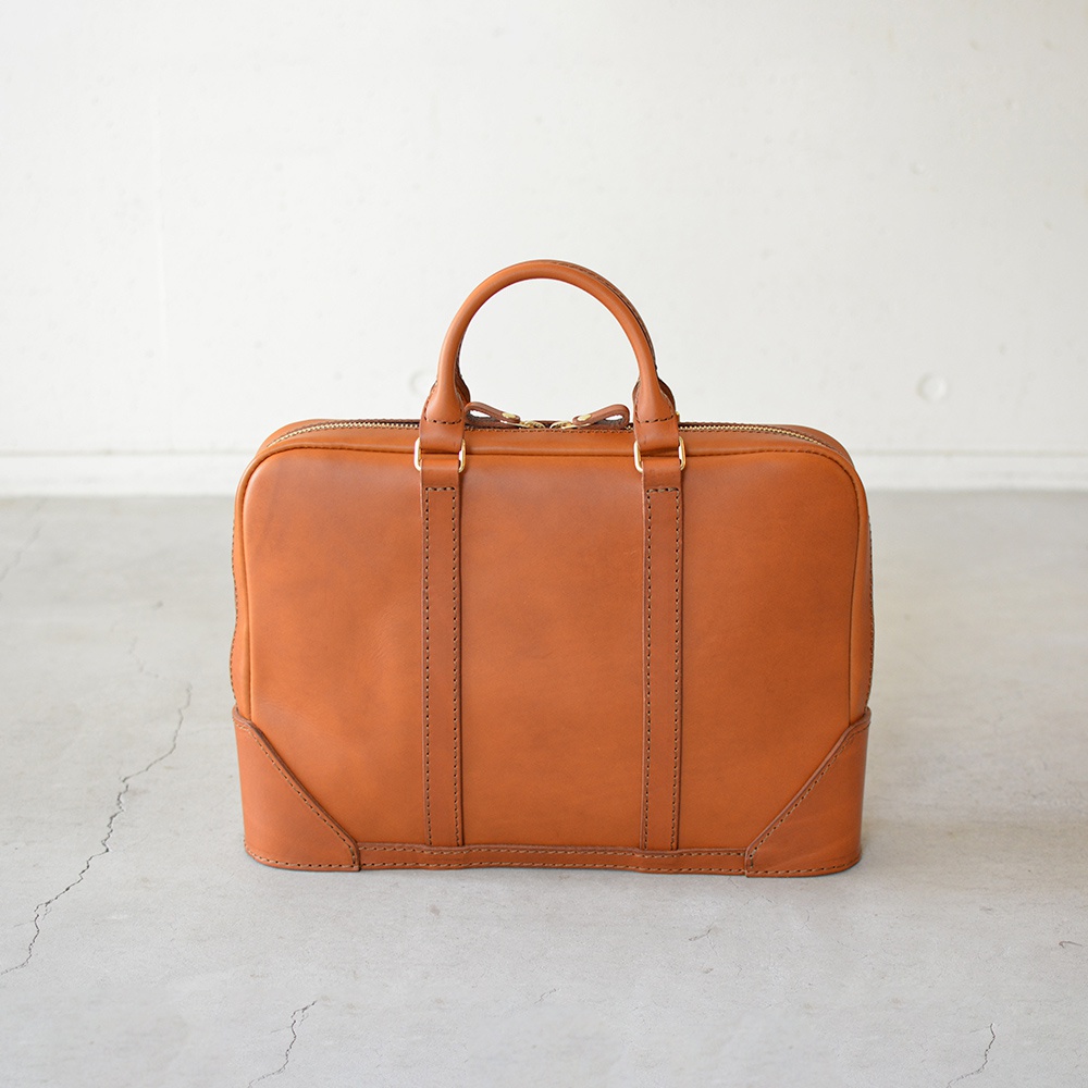 一個棕褐色皮革製的公事包，帶有頂部提把和拉鍊開口。包包表面有兩條垂直的縫線，底部邊角有加固設計。