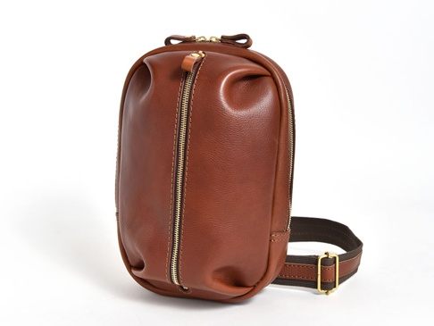 立體鞣製皮革運動斜背包，採用棕色調，配有金色拉鍊和織帶，整體設計簡潔大方。