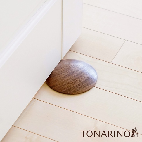 天然實木門擋，圓弧形狀，木紋清晰，深棕色澤，置於白色門板與淺色木地板之間，防止門撞擊牆壁。