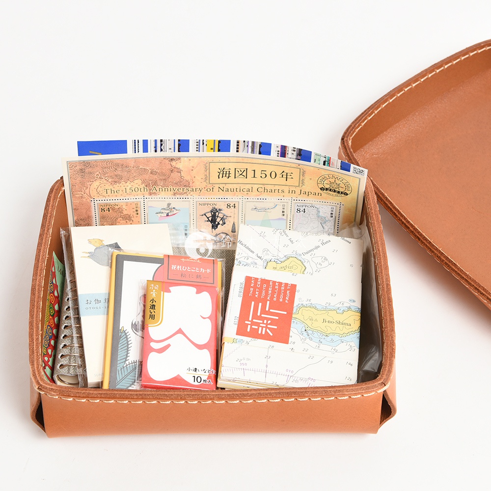 淺棕色皮革製成的手作收納盒，盒內裝有日本海圖、郵票、小卡及其他文具小物，盒蓋部分為可拆卸設計。