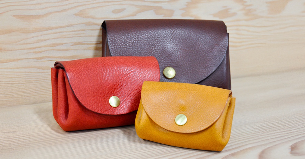 三款皮革零錢包，分別為紅色、黃色及深棕色，皆採用荔枝紋皮革材質，並配有金色按扣。