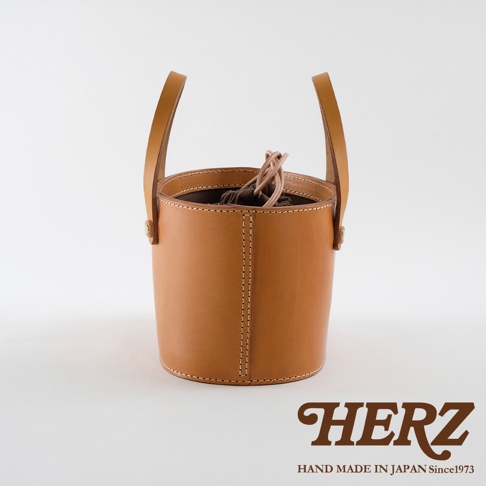 職人手作皮革束口手提包，採用天然皮革，經典圓筒造型，附有兩條短提把，束口處有抽繩設計，車線工整，展現皮革質感。