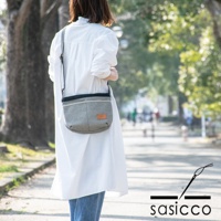 一位女性身穿白色長版上衣與牛仔褲，斜挎著一個黑色與白色細點圖案的三河木綿刺子織肩背包，包包上有一個淺棕色皮革標籤，揹帶為黑色鏈條。