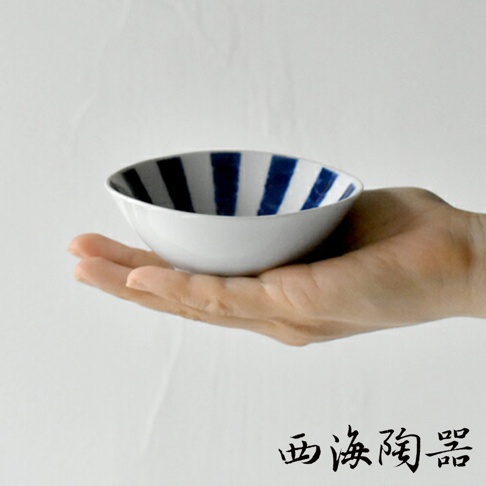 一隻手托著一個白色陶瓷小碗，碗內側有深藍色放射狀條紋。