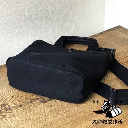 黑色帆布製成的兩用托特包，帶有皮革提把和可拆卸肩帶。包身結構紮實，底部為方形，材質為耐磨帆布。