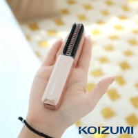 手持玫瑰金色迷你瀏海梳，梳齒為黑色，背景為模糊的黃色格紋布料。