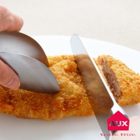 銀色金屬不沾桌調理幫手夾，夾著一塊炸至金黃的炸豬排，刀子正切斷豬排。