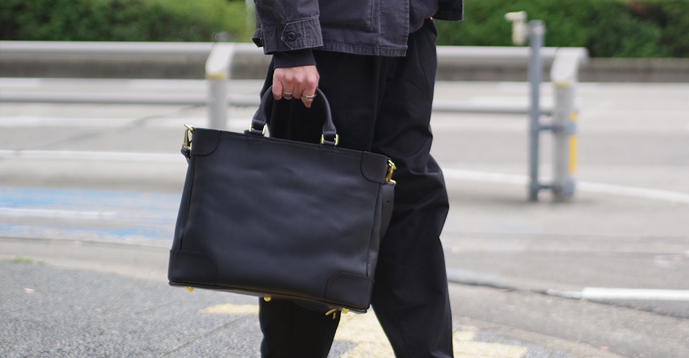 黑色皮革製成的兩用商務托特包，附有金色五金配件，可手提或肩背。