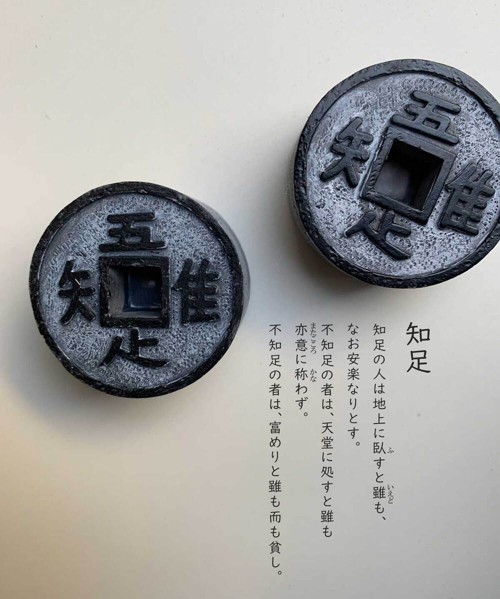 兩枚仿古錢幣模型，表面有「知」、「足」、「五」、「銖」等漢字，為深灰色帶有斑駁質感，中心為方形鏤空。