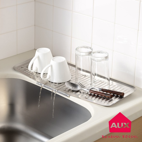 不鏽鋼長形瀝水籃上，擺放著兩個白色馬克杯、兩個透明玻璃杯，以及一支湯匙和叉子。瀝水籃的設計有助於水滴直接流入水槽。