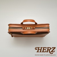 職人手作皮革兩用商務公事包，採用天然皮革材質，呈現溫潤的棕褐色調，配有雙拉鍊開合及頂部提把，簡約俐落的設計。