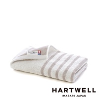 一條折疊的迷你浴巾，淺灰色與米白色條紋，毛圈材質，左側有 HARTWELL IMABARI JAPAN 品牌標籤。