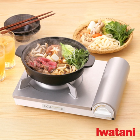 銀色節能高效瓦斯爐Eco Premium II CB-EPR-2，爐面上放置黑色鍋子，鍋內有牛肉、菇類、蔬菜、烏龍麵，冒著熱氣。旁邊有兩杯飲品、餐具及一籃食材。