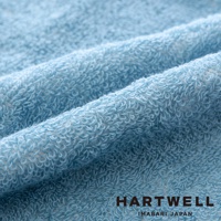 淺藍色毛巾布料，質地柔軟，紋理清晰，表面有細緻的毛圈，布料呈現自然的皺褶，印有 HARTWELL IMABARI JAPAN 字樣。