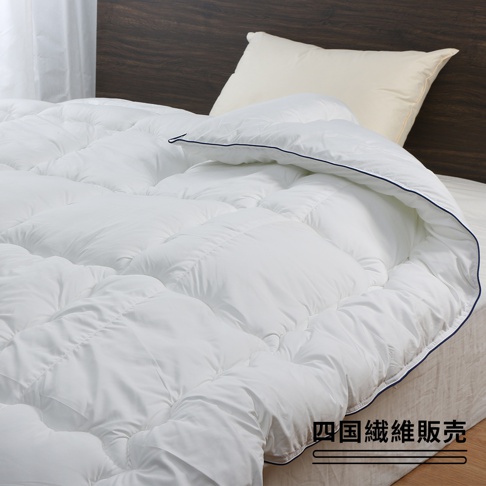 雙人SOFAIR無重力空氣被，輕柔的白色棉質，具有蓬鬆的紋理，邊緣有細緻的深藍色滾邊，覆蓋在床上，搭配一個米色枕頭和木質床頭板。