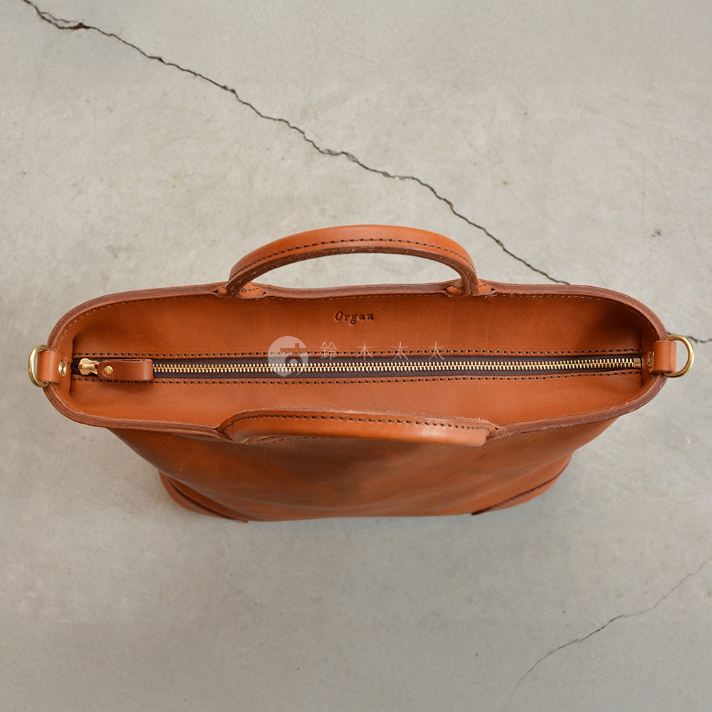 日本HERZ職人手作皮革Organ兩用拉鍊托特包，特寫棕色皮革包包上方拉鍊與提把，字樣「Organ」壓印其中