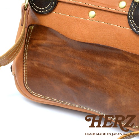 職人手作皮革郵差包，採用天然皮革製成，呈現棕色漸層紋理，以縫線和金屬釦點綴，設計簡約實用。