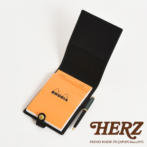 黑色皮革製的便利貼收納套，內含一本橘色 RHODIA 品牌的便利貼，並有一支綠色筆。